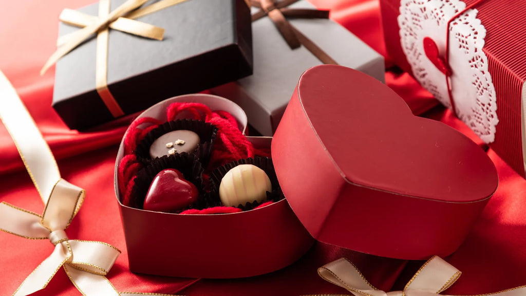 Una caja de bombones con forma de corazón junto a varios regalos de San Valentín